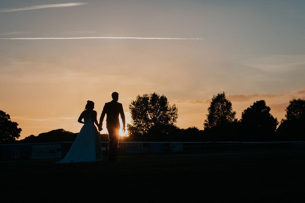 bride and groom holding hands in front of sunset