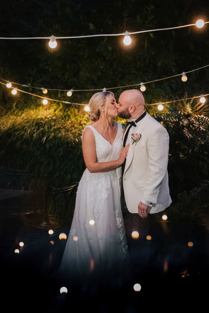 bride and groom kissing under festoon lights at night