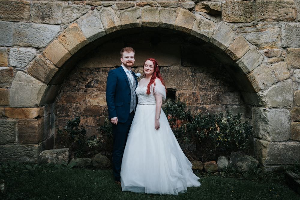 bride and groom in front of stone wall at Danby Castle