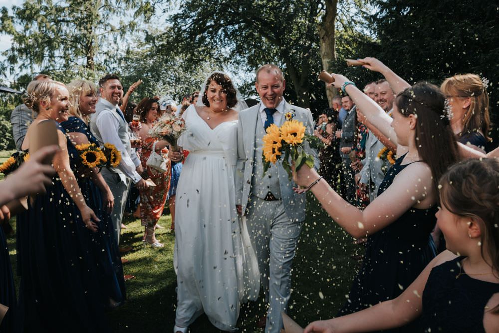 A bride and groom walking through confetti and Losehill House